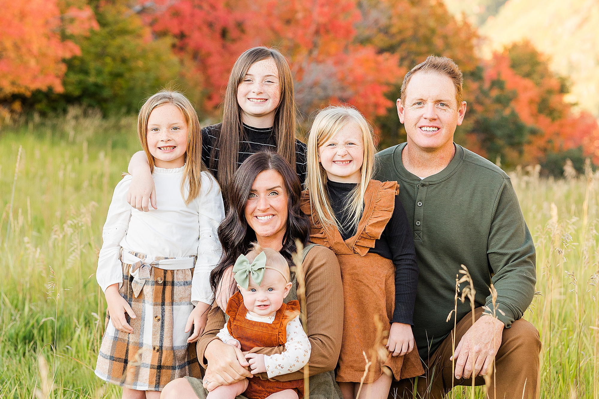 A happy family, all dressed in warm autumn colors, gathered in front of the Utah mountains.